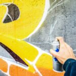 Detail of street artist painting colorful graffiti on public wall